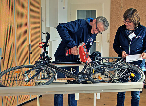 Fahrrad-Codierung Nadeldrucker Ein Mann codiert mit einem Nadeldrucker ein auf der Seite liegendes Fahrrad, während die Besitzerin zuschaut.